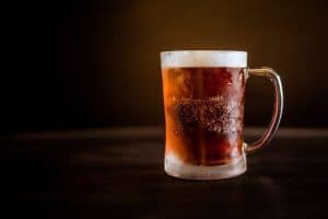La taza de cristal esmerilado, similar a las de Visita y cata en La Cervecería de Poblenou (Barcelona), rebosa de una bebida oscura y helada coronada de espuma cremosa sobre un fondo oscuro. - ForTwo - Planes para parejas