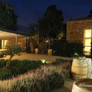 Bajo las estrellas del Hotel Lotus Priorat, el acogedor patio cuenta con una pérgola iluminada, plantas exuberantes, árboles imponentes y barriles rústicos contra un encantador muro de piedra. Ven a vivir la "Escapada de enoturismo de la mano del Hotel Lotus Priorat", rodeado de la belleza natural de Falset. - ForTwo - Planes para parejas