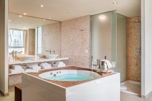 Disfrute de un lujoso y moderno baño en el Hotel con jacuzzi SB Diagonal Zero (Barcelona), con jacuzzi, lavabos dobles y una amplia ducha. Un gran espejo le aporta elegancia, y las toallas cuidadosamente dobladas realzan su estancia en este exquisito hotel. - ForTwo - Planes para parejas