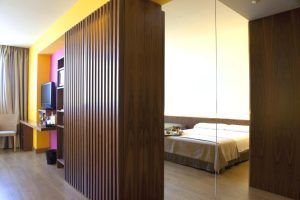 El Hotel con jacuzzi SB Diagonal Zero de Barcelona ofrece una elegante habitación con una moderna mampara de madera, televisor, escritorio y una cama con sábanas beige. Reflejado con elegancia en una pared de espejo, podrá relajarse aún más en el lujoso jacuzzi para una estancia inolvidable. - ForTwo - Planes para parejas