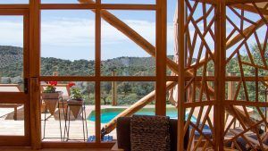 Contemple a través de las ventanas con marco de madera el patio con piscina privada, exuberante vegetación y ondulantes colinas en la Cabaña Junior Suite con piscina privada de La Dehesa Experiences (Córdoba). Disfrute de esta tranquila escapada. - ForTwo - Planes para parejas