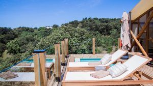 Dos tumbonas junto a la piscina en un deck de madera ofrecen un escape tranquilo, con vista a la exuberante vegetación bajo un cielo azul claro, perfecto para disfrutar de la Cabaña Junior Suite con Piscina Privada en La Dehesa Experiences en Córdoba. - ForTwo - Planes para parejas