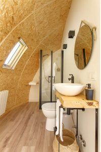 Transforma tu baño en un oasis moderno y elegante inspirado en los Iglús panorámicos en plena Selva de Irati (Navarra), con suelo de madera, lavabo ovalado, espejo redondo y un techo de madera curvado que personifica la elegancia natural. - ForTwo - Planes para parejas