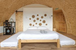 Un acogedor dormitorio con techo de arco de madera, ropa de cama blanca y detalles circulares en la pared sobre la cama evoca el encanto tranquilo del "Iglús panorámicos en plena Selva de Irati (Navarra). - ForTwo - Planes para parejas