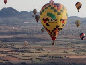 Los globos aerostáticos flotan sobre un pintoresco paisaje de Mallorca con majestuosas montañas, ofreciendo una experiencia mágica con el "Vuelo en globo privado para dos al amanecer (Mallorca). - ForTwo - Planes para parejas