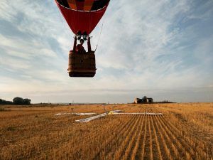 Un globo aerostático aterriza en un campo cosechado con un marcador en el suelo bajo un cielo parcialmente nublado, ofreciendo la experiencia de "Vuelo en globo privado para dos al amanecer" que recuerda los serenos paisajes de Mallorca. - ForTwo - Planes para parejas
