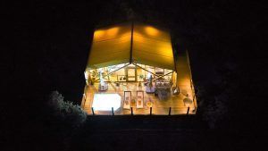 Vista aérea nocturna de una cabaña cálidamente iluminada con piscina, enclavada entre la vegetación oscura, disponible por 2 noches en La Dehesa Experiences en Córdoba. Incluye cena, desayuno y decoración romántica. - ForTwo - Planes para parejas