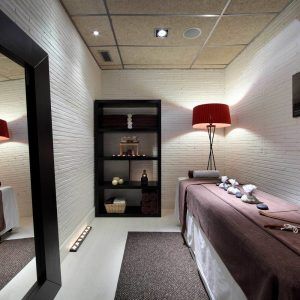 Disfrute de una tranquila experiencia de spa en el circuito Almuerzo, que cuenta con una sala de masajes con cama, estante, lámpara y toallas y piedras cuidadosamente dispuestas. - ForTwo - Planes para parejas