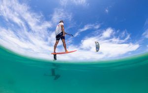 Un aficionado al kitesurf se desliza sobre las aguas turquesas de Tarifa bajo un cielo azul con nubes blancas, mientras que Subcielo KiteSchool Tarifa (Cádiz) ofrece el "Curso de KiteSurf para dos personas" para aquellos deseosos de dominar las olas. - ForTwo - Planes para parejas
