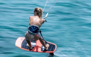 Una persona practicando kitesurf en la costa de Tarifa en aguas turquesas, con arnés y vistiendo pantalones cortos coloridos del "Curso de KiteSurf para dos personas" de Subcielo KiteSchool, crea una estela impresionante detrás de la tabla. - ForTwo - Planes para parejas