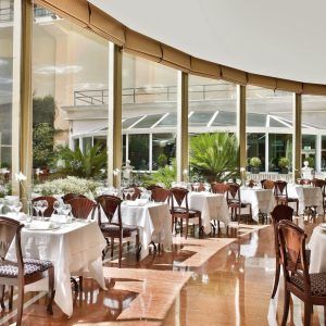 Restaurante elegante con ventanas curvas y mesas puestas, que ofrece una tranquila vista al jardín. Ideal para disfrutar del "Masaje y almuerzo ejecutivo a la carta" en el Hotel InterContinental Gran Vía, Madrid. - ForTwo - Planes para parejas