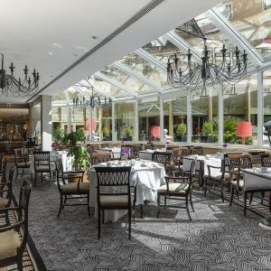 Disfrute de un sofisticado almuerzo ejecutivo en el Hotel InterContinental Gran Vía de Madrid, que cuenta con un ambiente refinado con techos de cristal, lámparas de araña y mesas elegantemente dispuestas con manteles blancos. - ForTwo - Planes para parejas
