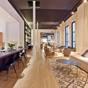 Moderna sala de estar de planta abierta con pisos de madera clara, asientos acogedores, comedor perfecto para una experiencia de almuerzo y una isla de cocina negra con sillas. - ForTwo - Planes para parejas