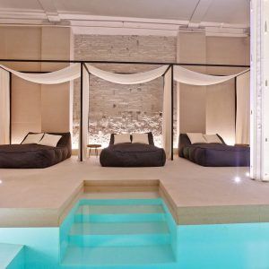 Experimente el lujo en el Almuerzo, Spa y Masaje con aceites veganos del hotel Yurbban en Barcelona, que cuenta con una sala de spa con tres tumbonas acolchadas, cortinas blancas y una piscina turquesa para el mejor masaje relajante. - ForTwo - Planes para parejas