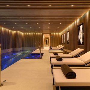 La lujosa piscina cubierta del Hotel Seventy Barcelona cuenta con tumbonas, un techo de madera y una iluminación suave que crean un ambiente de spa sereno realzado por relajantes aceites de masaje veganos con aromaterapia. - ForTwo - Planes para parejas