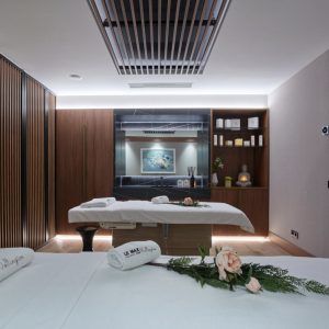 Relájese en la tranquila sala de tratamientos del Wellington Hotel Spa de Madrid. Con dos camillas de masaje, toallas enrolladas y flores rosas sobre elegantes detalles de madera, es su refugio ideal. - ForTwo - Planes para parejas