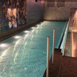 La Oferta: circuito de spa en Wellington Hotel Spa (Madrid) incluye una piscina cubierta con agua iluminada, barandilla metálica, paredes texturizadas y arte abstracto de fondo. - ForTwo - Planes para parejas