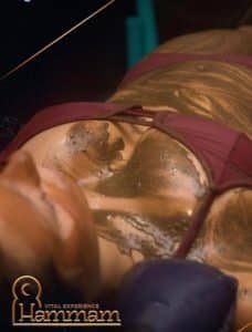 Una persona en bikini cubierta de arcilla dorada se relaja en un lujoso spa, disfrutando del rejuvenecedor Baño turco para parejas en Madrid (Hammam Vital Experience), que ofrece una escapada ideal para parejas que desean tranquilidad en el mejor refugio de Madrid. - ForTwo - Planes para parejas