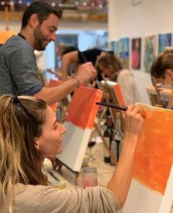 En un estudio luminoso, los participantes de la Clase de pintura con tu copita de vino en Arte Bar (Barcelona) se concentran intensamente en su obra de arte, pintando sobre lienzos para capturar el espíritu vibrante de Barcelona. - ForTwo - Planes para parejas