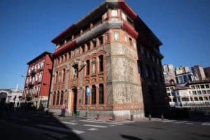 El adornado edificio histórico con ventanas arqueadas en Bilbao es un lugar majestuoso en una esquina de la calle bajo un cielo despejado, lo que lo convierte en una parada intrigante en cualquier tour gratuito alternativo que explore la mezcla tradicional y moderna de la ciudad. - ForTwo - Planes para parejas