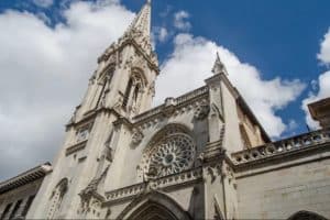 Contra un cielo azul parcialmente nublado se alza una catedral alta y ornamentada con una aguja, una vista pintoresca para los visitantes de Bilbao, que se disfruta mejor en el "Tour gratuito por Bilbao". - ForTwo - Planes para parejas