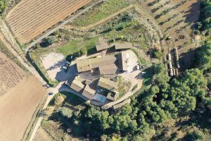 Vista aérea de un conjunto de edificios rústicos rodeados de campos y árboles, ideal para vivir la tranquila experiencia "Visita a bodega con degustación y cata de vinos Miquel Jané" en Barcelona. - ForTwo - Planes para parejas