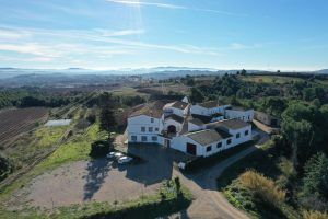 Vista aérea de una finca rural con edificios blancos y campos bajo un cielo azul claro, ideal para una visita tranquila a la Bodega Miquel Jané con cata de vinos y degustación en Barcelona. - ForTwo - Planes para parejas