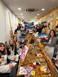 Los participantes en un evento de Wine Gogh - Pintar mientras bebes vino en Barcelona, sosteniendo pinturas y copas de vino, sonríen y posan para una foto de grupo. - ForTwo - Planes para parejas