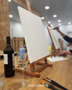 Un lienzo en blanco sobre un caballete, con una botella de vino y una copa sobre la mesa, prepara el escenario en el estudio de arte, invitando a la creatividad inspirada en Wine Gogh - Pintar mientras bebes vino (Barcelona). - ForTwo - Planes para parejas