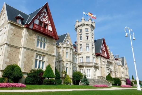 La visita al Palacio de la Magdalena en Santander muestra banderas en lo alto de una torre, contra un cielo azul claro y rodeadas de exuberante vegetación. - ForTwo - Planes para parejas