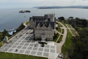 Desde una vista aérea, la Visita al Palacio de la Magdalena (Santander) revela su majestuosidad junto al mar, rodeada de frondosos senderos y vegetación. Esta joya histórica es una visita obligada en la encantadora ciudad costera. - ForTwo - Planes para parejas