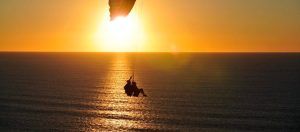 La silueta de un parapente se desliza con gracia contra el fondo del océano al atardecer, creando una escena impresionante con un horizonte dorado. ¿Podría ser esta serena vista de "Vuelo en parapente biplaza en Vejer (Cádiz)"?. - ForTwo - Planes para parejas