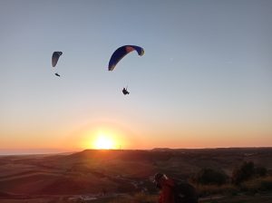 Dos personas disfrutan de un vuelo en parapente biplaza en Vejer (Cádiz) al atardecer, elevándose sobre el paisaje montañoso y la impresionante costa. - ForTwo - Planes para parejas