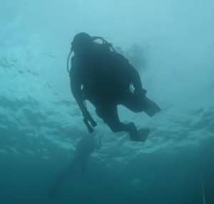 Un buceador se desliza por las cristalinas aguas de Cantabria, mientras otro explora las profundidades al fondo, cerca de Castro Urdiales, un lugar ideal para que los entusiastas experimenten un bautismo de buceo. - ForTwo - Planes para parejas