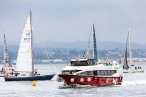 Un velero y una lancha a motor se deslizan por el mar tranquilo y nublado cerca de la costa de Santander, ideal para un paseo en barco en Santander. - ForTwo - Planes para parejas