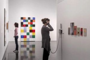 En el Museo de Arte Contemporáneo de Barcelona, un visitante admira una cuadrícula de colores mientras otro mira absorto con auriculares una exposición. - ForTwo - Planes para parejas