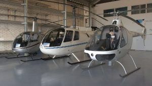Tres aviones "Vuelo en helicóptero por la Costa del Sol (Marbella)" están estacionados en el suelo de un hangar gris, listos para llevarte a unas vistas impresionantes. - ForTwo - Planes para parejas