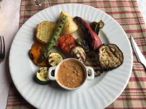 Verduras asadas y salsa cremosa reposan elegantemente sobre un plato blanco, colocado sobre un mantel a cuadros que recuerda a Almuerzo y visita a la bodega Mas Llunes en Garriguella, Girona. - ForTwo - Planes para parejas