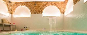 Disfrute de una lujosa piscina cubierta con arcos de ladrillo y cascada en el Spa Bodyna Hospes Puerta de Alcalá, ideal para relajarse después de una romántica cena para dos en Madrid. - ForTwo - Planes para parejas