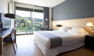 Alójese en el Hotel Món de 4 estrellas y disfrute de una combinación de confort moderno y encanto medieval. Disfrute de una habitación con cama grande, escritorio, televisor y balcón con vistas a la exuberante vegetación. En las inmediaciones, sumérjase en la historia del Monasterio de Sant Benet para vivir una experiencia inolvidable en el Bages, Barcelona. - ForTwo - Planes para parejas