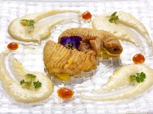 El Menú degustación con Estrella Michelin en el restaurante Nectari (Barcelona) presenta un plato elegante con pescado frito, puré blanco cremoso, puntos de salsa roja y una guarnición de flores moradas en un plato transparente. - ForTwo - Planes para parejas