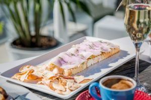 Saborea "El brunch de Óscar" en el hotel Room Mate Óscar, Madrid: un plato rectangular de pescado en rodajas sobre tostadas con patatas fritas, vino espumoso y café en un ambiente elegante. - ForTwo - Planes para parejas