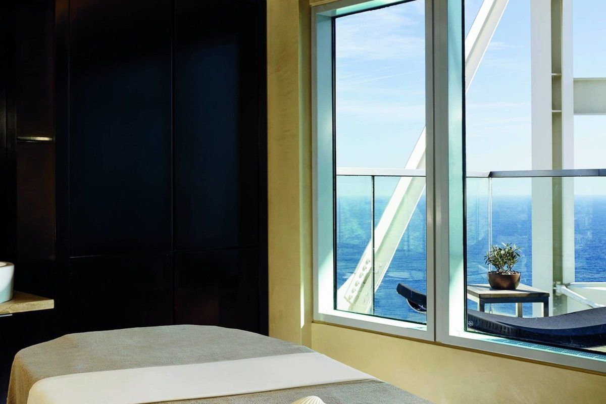 Disfrute del Desayuno, Spa de Lujo y Masaje: La Experiencia Total en el Hotel Arts, que cuenta con una relajante sala de spa con mesa de masajes, una gran ventana con vista al mar y una planta en maceta: un escape perfecto. - ForTwo - Planes para parejas