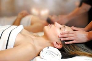 En el Meliá Barcelona Sky, una mujer disfruta de un relajante masaje de cabeza con toallas como parte de la experiencia Desayuno Buffet, Circuito Spa y Masaje en pareja en Serena Spa, posiblemente soñando con el desayuno buffet que le espera después. - ForTwo - Planes para parejas