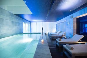Relájese en nuestra piscina cubierta del Spa en Hospes Palacio de los Patos (Granada), con tumbonas bajo un techo estrellado. Las paredes azules y la iluminación ambiental crean un ambiente tranquilo que refleja la esencia relajante del famoso spa de Granada. - ForTwo - Planes para parejas