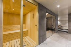 La sauna del Hotel Cataluña cuenta con bancos de madera y una puerta de cristal que da acceso a una zona de relax con tumbonas, ideal después de disfrutar del "Circuito de aguas, cava y masaje de esencias para parejas en Hotel Cataluña (Granada). - ForTwo - Planes para parejas