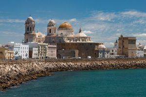 Disfrute de una vista costera de la Catedral de Cádiz, con sus majestuosas cúpulas elevándose cerca del paseo marítimo, bajo la hermosa luz del sol. Únase a un "Tour gratuito por Cádiz" para apreciar plenamente esta maravilla arquitectónica en un día soleado. - ForTwo - Planes para parejas