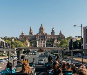 Los turistas en un autobús descapotable, con el Barcelona City Pass en la mano, admiran un gran edificio con cúpulas y agujas bajo el cielo soleado de Barcelona. - ForTwo - Planes para parejas