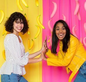 Dos mujeres chocan los cinco frente a un fondo vibrante con plátanos colgantes, capturando la esencia animada de Entradas Museo Big Fun Barcelona. - ForTwo - Planes para parejas
