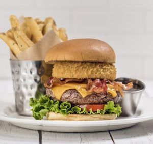 Disfruta de la Hamburguesa en Hard Rock Café Barcelona: una jugosa hamburguesa con queso, beicon y una crujiente rodaja de cebolla en un pan suave con lechuga fresca y tomate. Servida con patatas fritas crujientes y una sabrosa salsa para untar, el capricho perfecto. - ForTwo - Planes para parejas